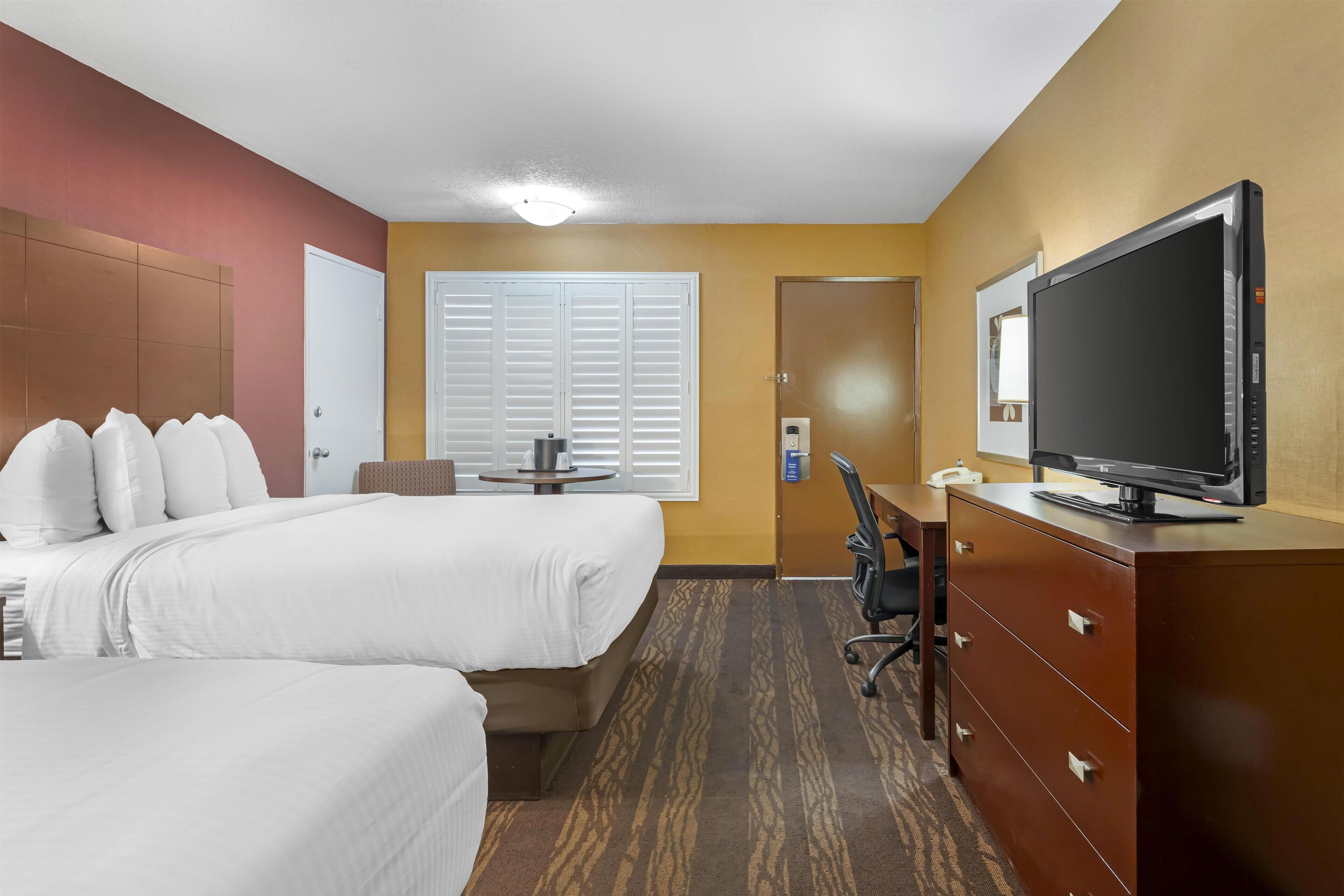A hotel room with two beds, a desk, a television, and a wardrobe.