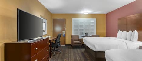 A hotel room with a TV on a dresser, a desk with a chair, two beds, and a window with blinds.
