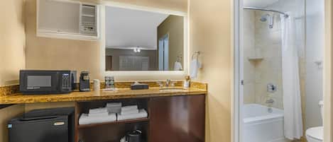 A hotel bathroom with a shower, toilet, sink, and a microwave on the countertop.