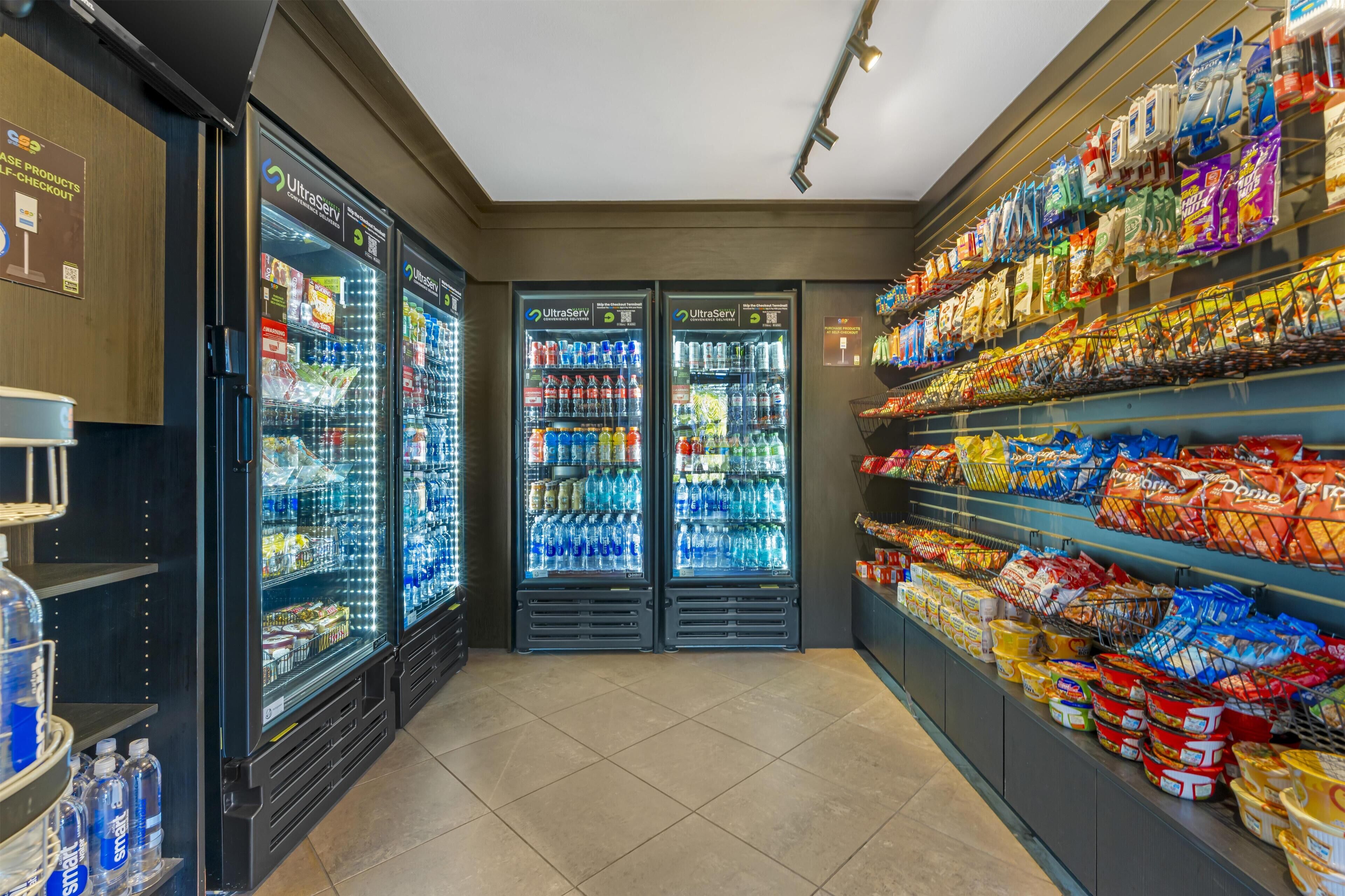 A self-checkout area with refrigerated beverage dispensers and shelves stocked with snacks and beverages.
