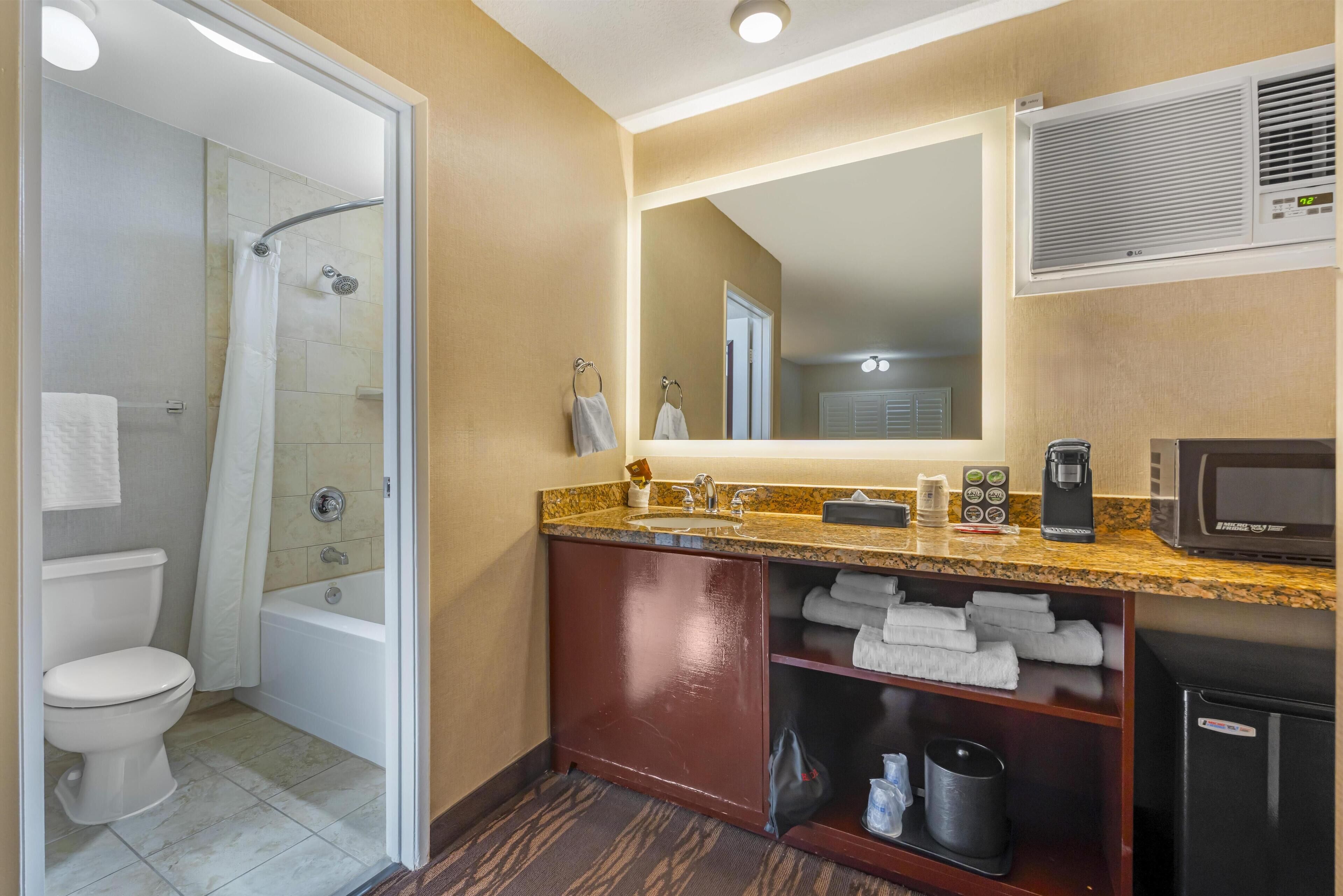 A hotel bathroom with a glass-enclosed shower, a sink with a mirror, and a cabinet with towels.