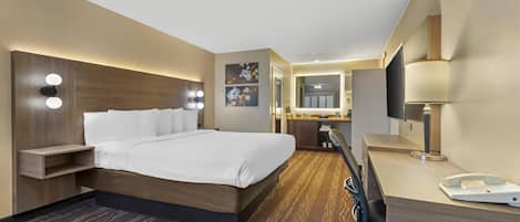 A hotel room with a large bed, bedside table with lights, a desk with a chair, and a TV.