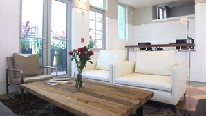 A modern living room with a wooden coffee table, a white sofa, and a chair. There is a vase with flowers on the table. - Leslie Hotel Ocean Drive (Miami Beach)