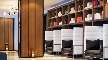 Una biblioteca moderna con filas de sillones de cuero blanco, estanterías de madera y una lámpara de techo original.