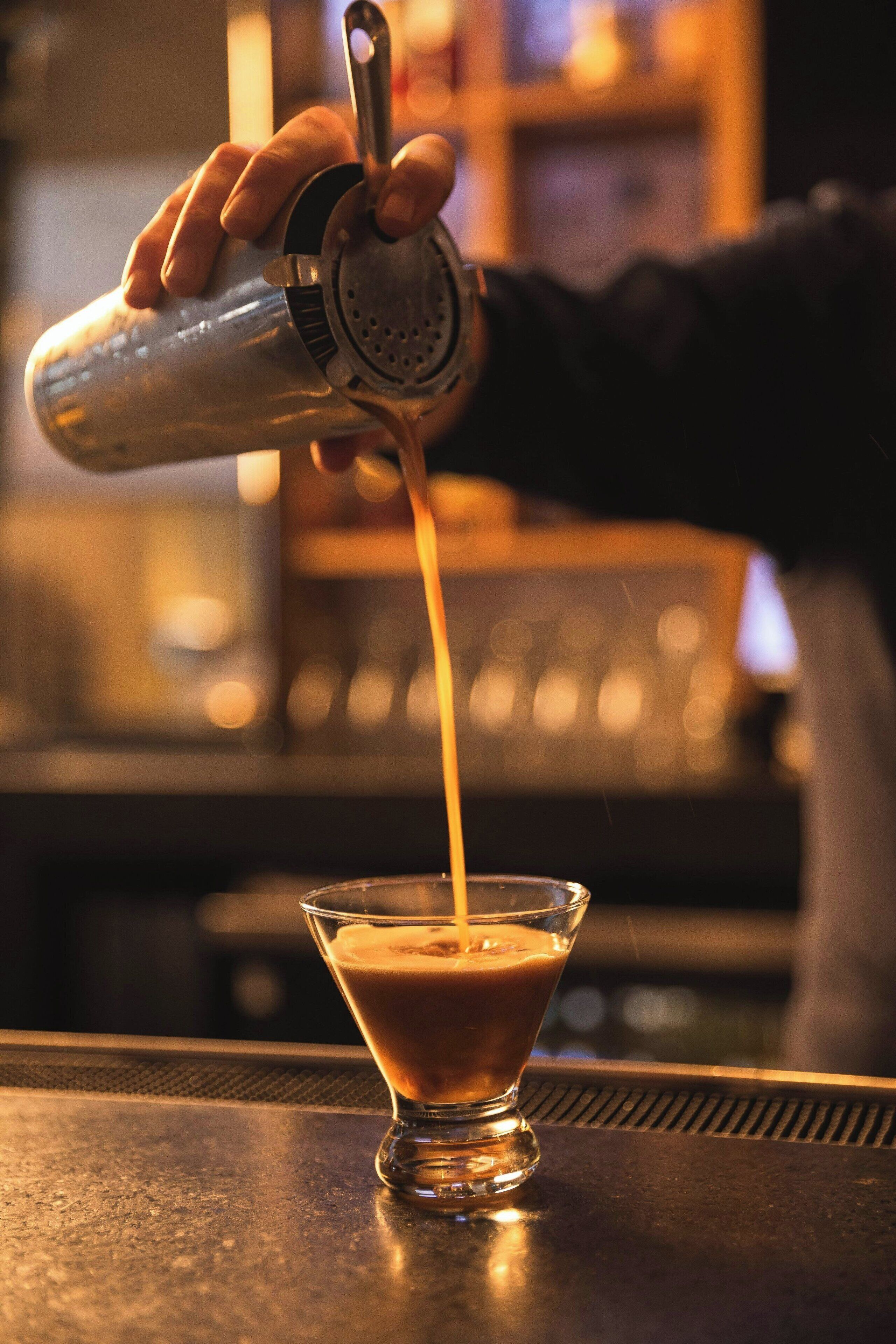 A bartender pouring a drink into a martini glass.