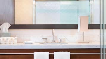 A modern bathroom with a marble countertop, a large mirror, a towel rack, and a sink with two faucets.