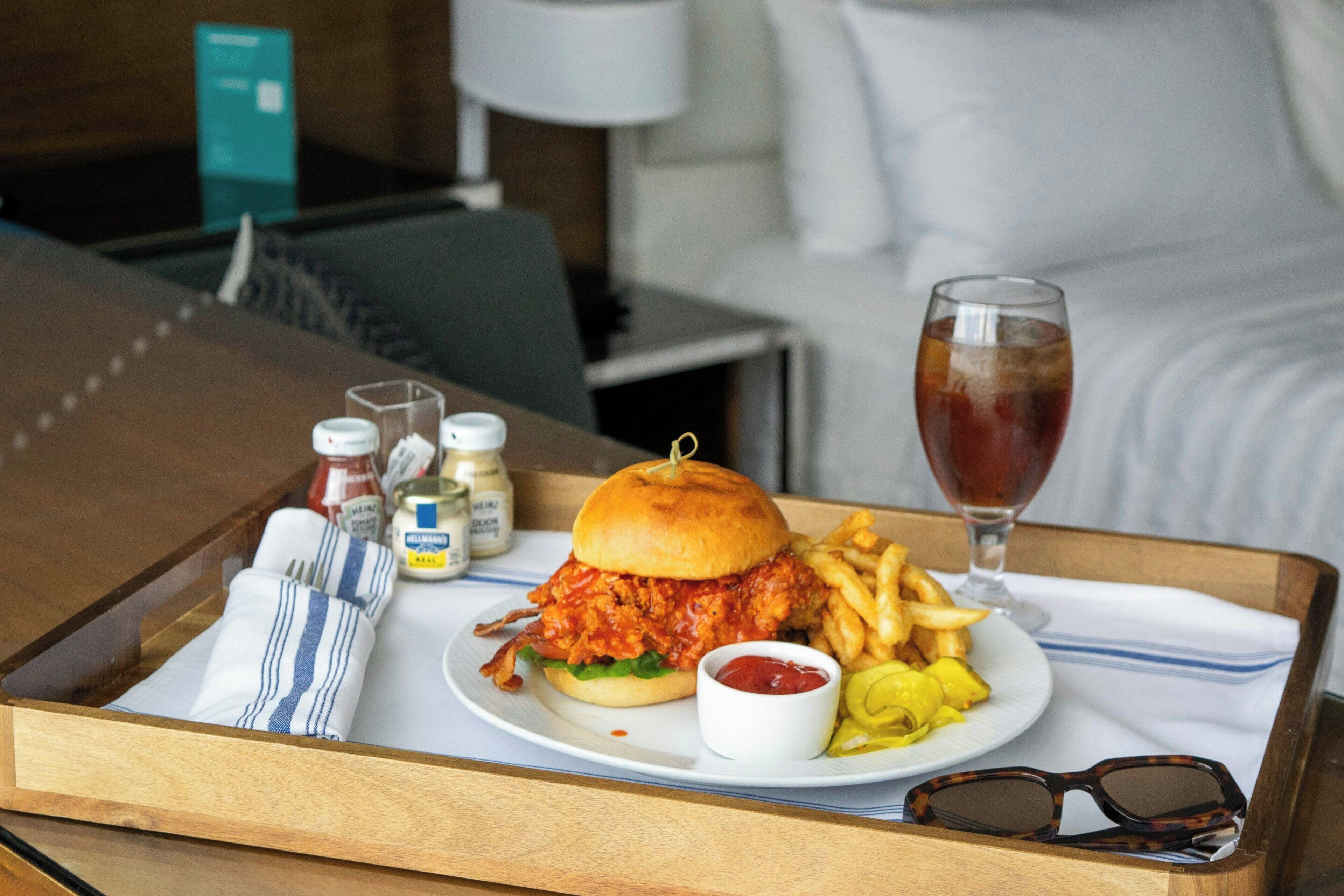 A tray with a chicken sandwich, fries, ketchup, and a drink on a hotel table.