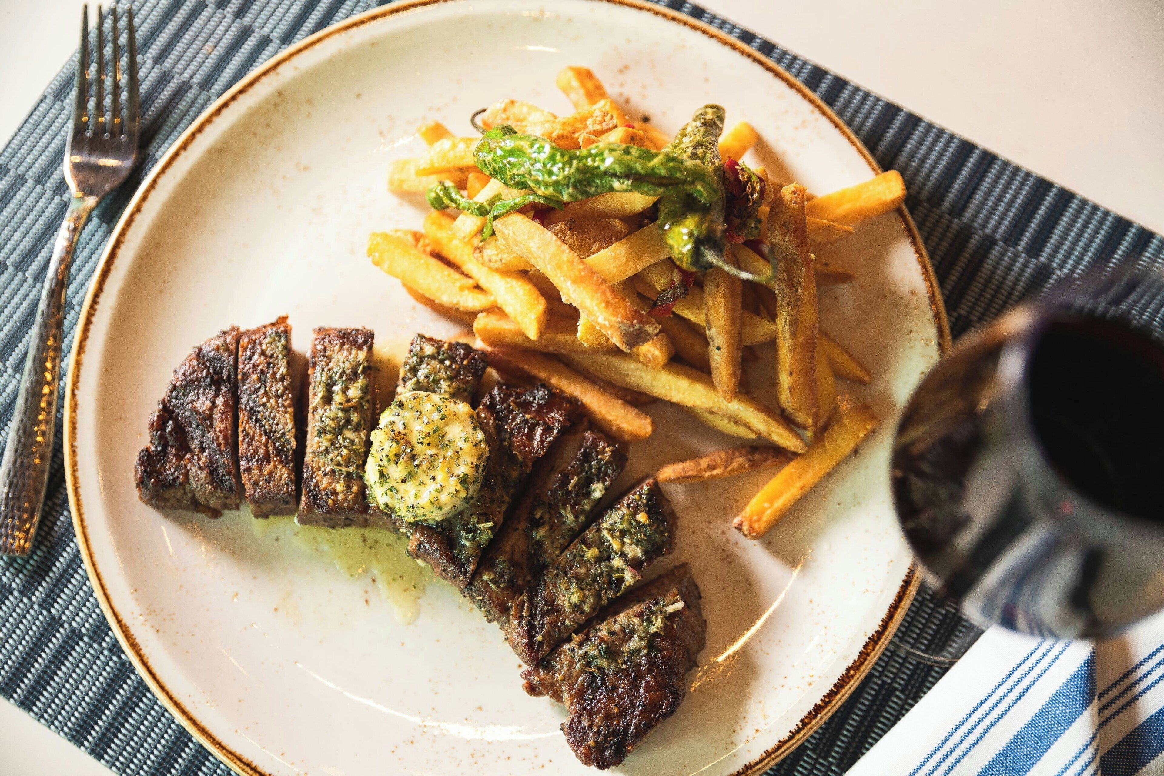A plate with steak and fries, a fork, and a glass of beverage.
