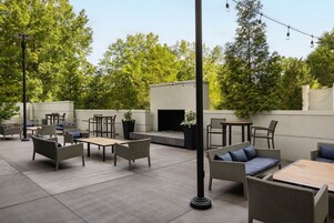 An outdoor patio area with multiple seating arrangements, including sofas and tables, surrounded by greenery and trees.