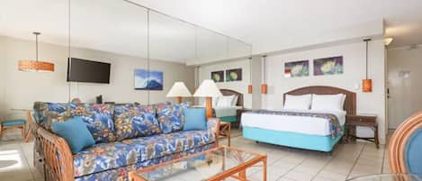 Una habitación de hotel con un sofá, una cama, una mesa de centro de vidrio y una televisión.