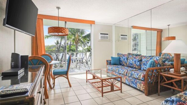 A hotel room with a balcony, a sofa, a coffee table, and a TV.