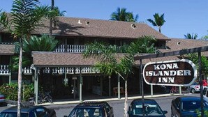 A hotel named Kona Islander Inn with a two-story structure, a covered outdoor area with a railing, and several cars parked in front.