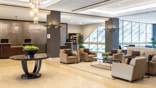 A modern lobby with a reception desk, seating area, and a view of the sky through large windows.