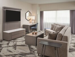 Una habitación de hotel moderna con televisión de pantalla plana, un escritorio con silla, un sofá y una mesa de centro.