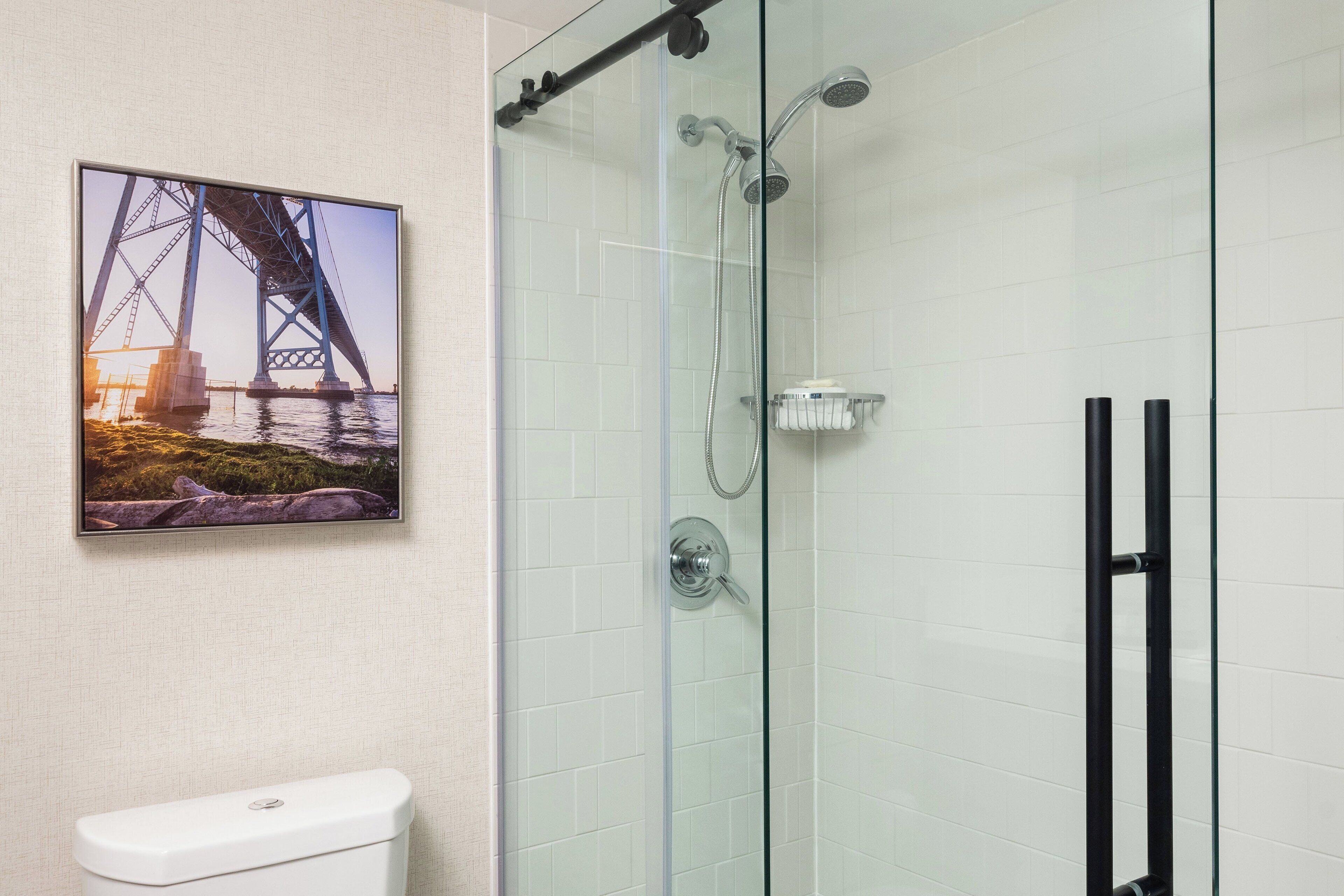 A bathroom with a glass shower enclosure, a toilet, and a framed picture of a bridge.