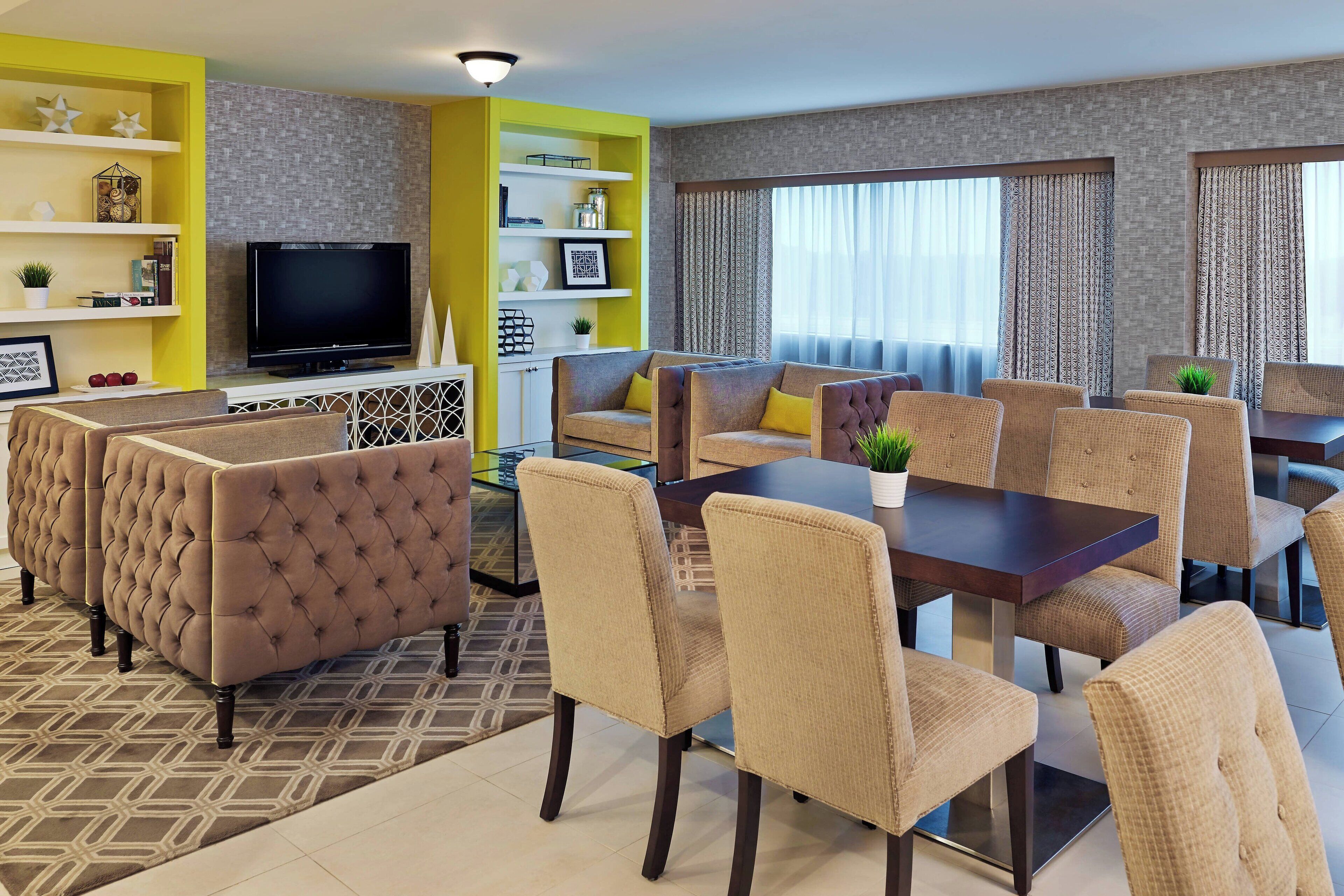 Una sala de estar moderna con un sofá seccional, una mesa de comedor con sillas, un televisor de pantalla plana y estanterías decorativas.