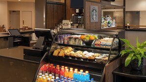 A hotel lobby with a coffee bar, a seating area, and a counter with various beverages and pastries.