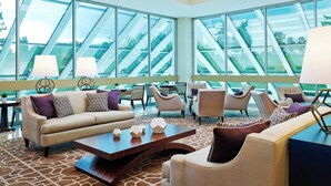 A modern hotel lobby with a large glass window wall, comfortable seating, and a geometric patterned rug.
