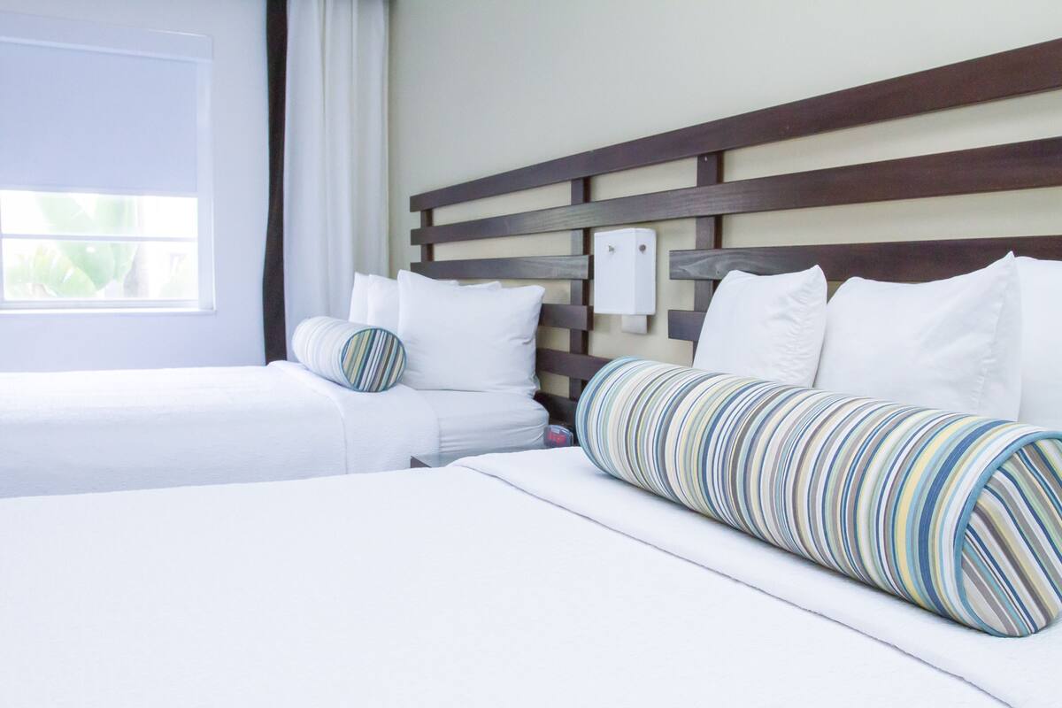A hotel room with two beds, a wooden headboard, white bedding, and a striped pillow.
