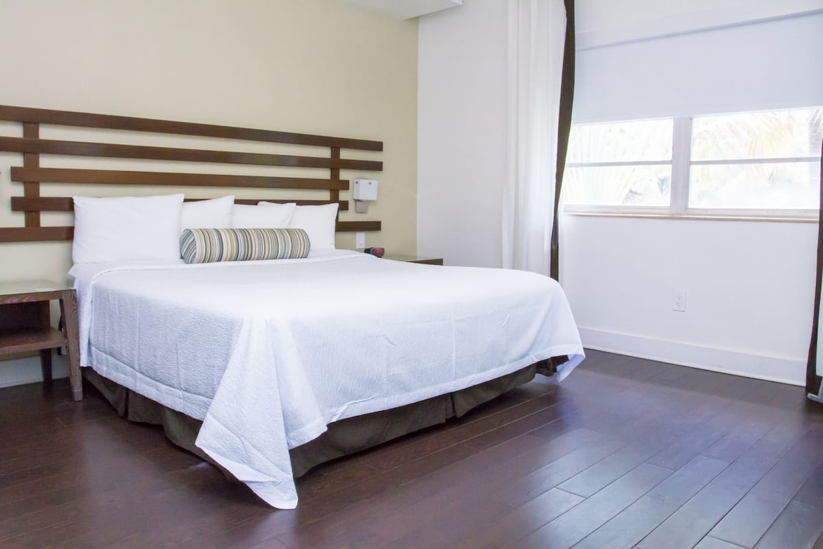 A neatly made bed with a wooden headboard, a bedside table, and a window with curtains.