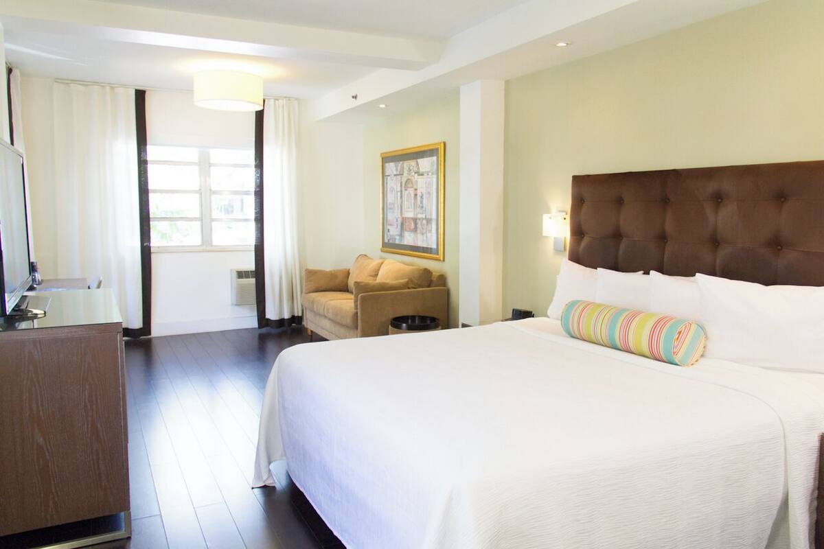 A hotel room with a large bed, a sofa, a television, and a painting on the wall.