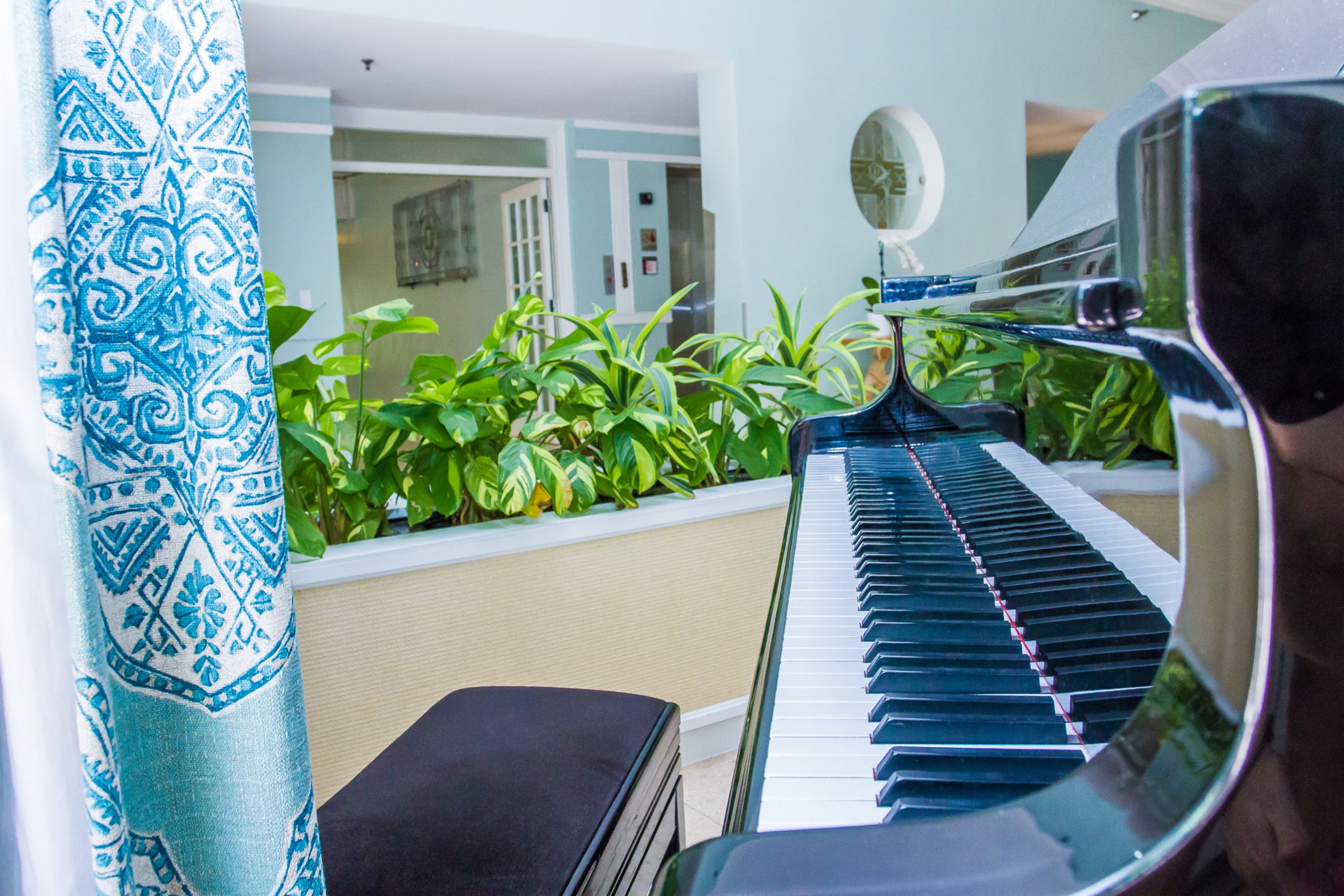 Un piano en una habitación con cortina estampada, un espejo y plantas verdes.
