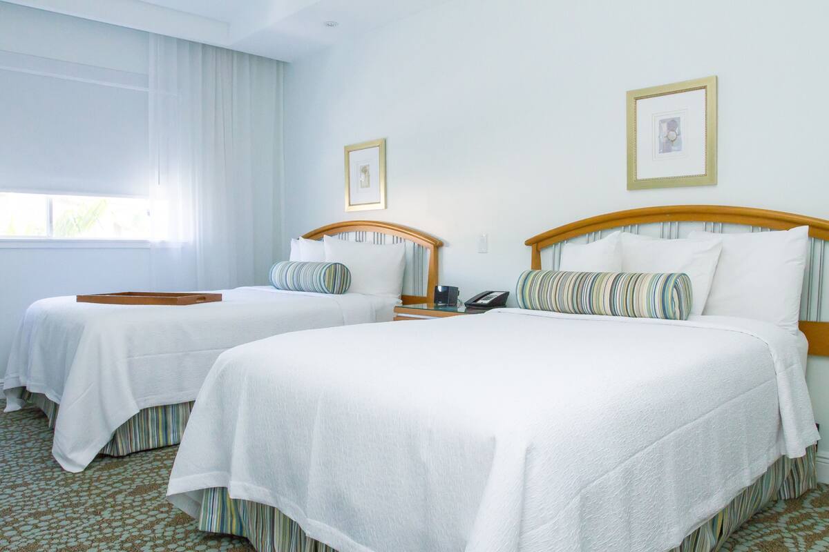 A hotel room with two beds, a bedside table with a phone, and a window with curtains.