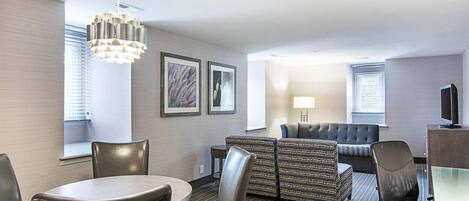 Habitación de hotel con una mesa de comedor, sillas, un sofá, un televisor y obras de arte en las paredes.