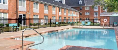 A swimming pool with a metal ladder, surrounded by a brick building with multiple windows and a fence.