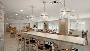 A spacious dining area with a long table and multiple chairs, elegant crystal chandeliers, and a modern kitchen in the background. - Comfort Inn Williamsburg Gateway (Williamsburg)
