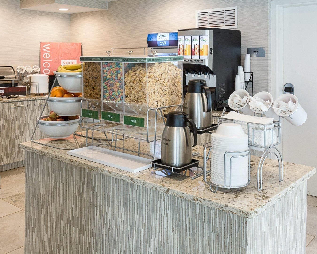 A self-service breakfast station with cereal, fruits, and coffee options.