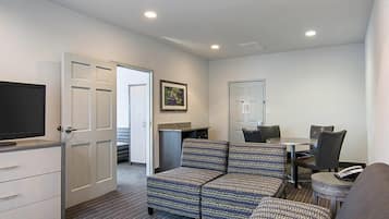 A compact living space with a television, sofa, dining table, chairs, and a small kitchenette.