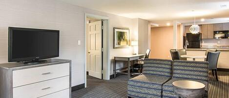 Une chambre d’hôtel équipée d’un téléviseur à écran plat, d’un canapé, d’une table à manger avec des chaises, d’un petit coin cuisine et d’une porte donnant sur une autre pièce.
