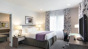 A hotel room with a bed, two bedside lamps, a desk with a TV, a chair, and a window with curtains.