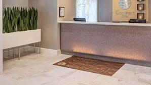 A reception area with a modern design, featuring a reception desk, a framed welcome sign, and a decorative wall with framed pictures. - Comfort Inn Williamsburg Gateway (Williamsburg)