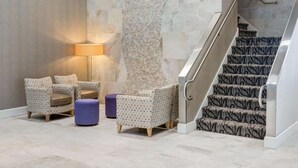 A lobby with a staircase, patterned chairs, a lamp, and a textured wall. - Comfort Inn Williamsburg Gateway (Williamsburg)
