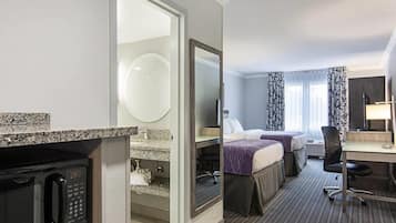 A hotel room with a kitchenette, two beds, a desk, and a large mirror.