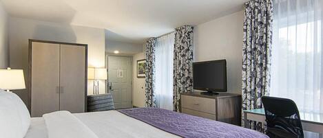 Ein Hotelzimmer mit einem Bett, einem Schreibtisch mit Computer, einem Fernseher und einem Sessel.