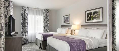 Habitación de hotel con dos camas, televisión y ventana con cortinas.