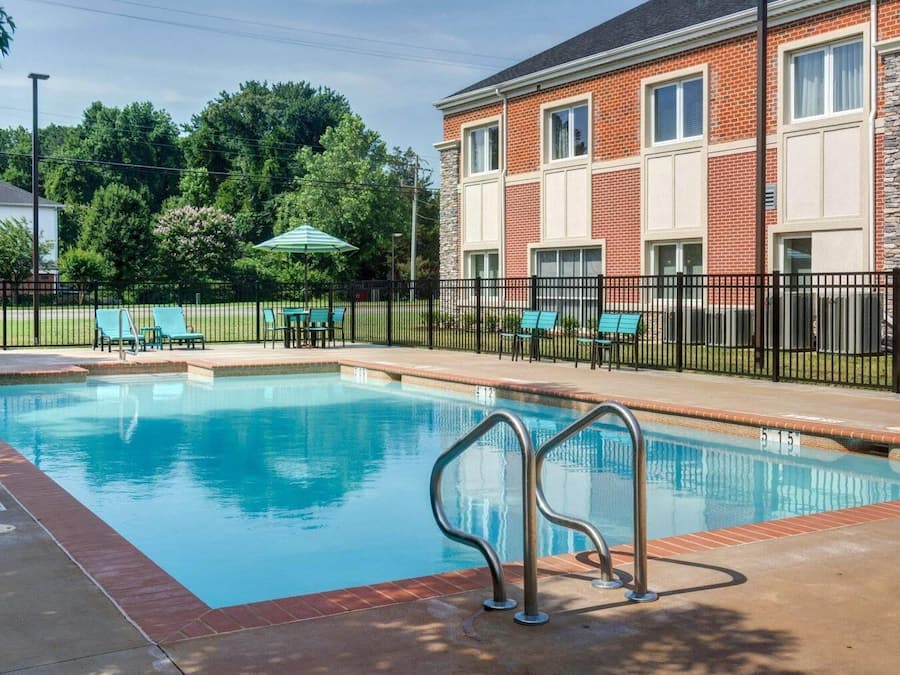 A swimming pool with a metal ladder, surrounded by a brick building with windows and a black fence.