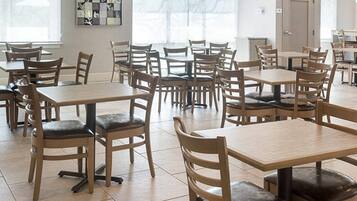 Un comedor amplio con varias mesas y sillas, ventanas grandes con cortinas translúcidas y una obra de arte abstracta colgada en la pared.