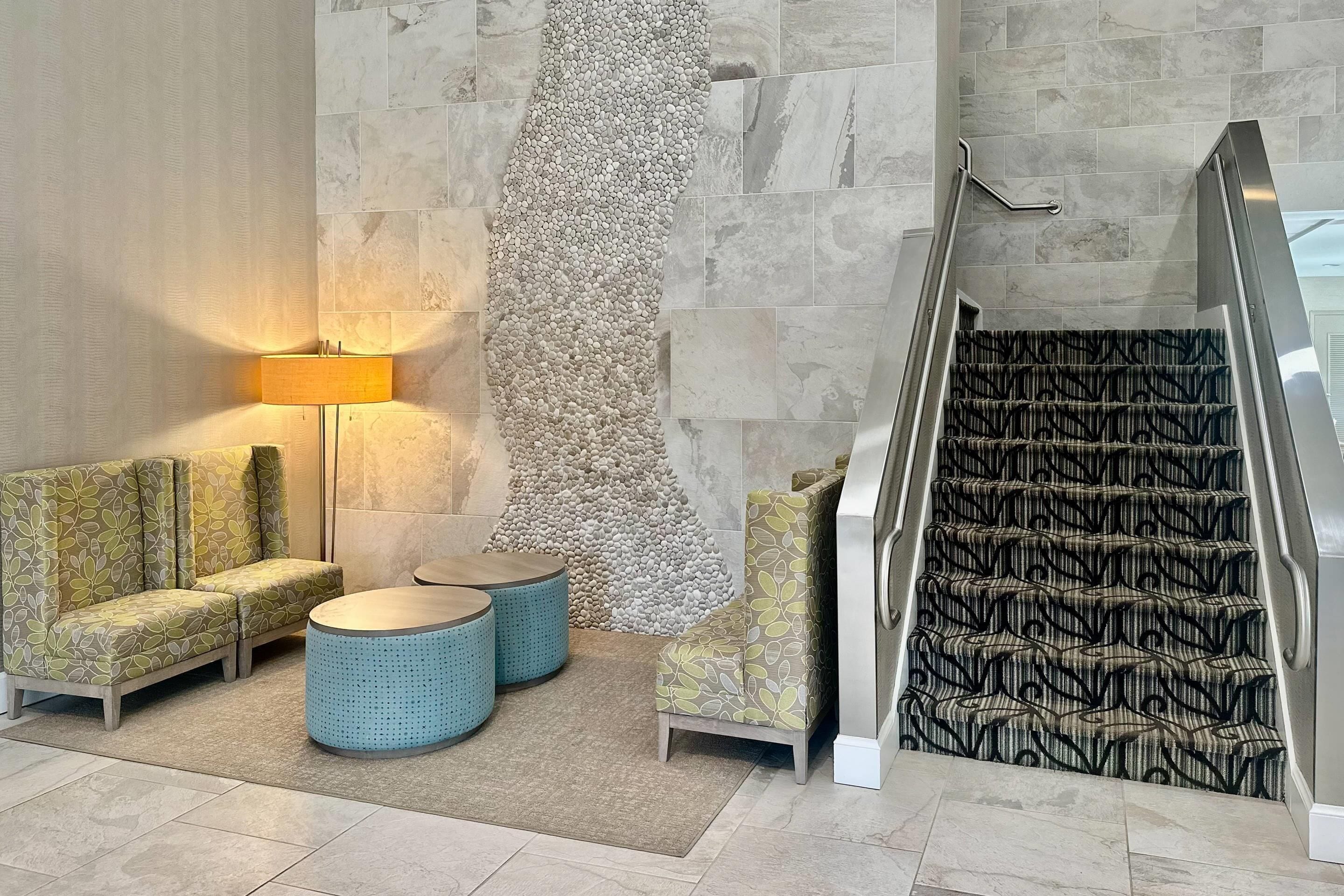 Eine Lobby mit einer Couch, zwei runden Tischen, einer Lampe, einer strukturierten Wand und einer gemusterten Treppe.