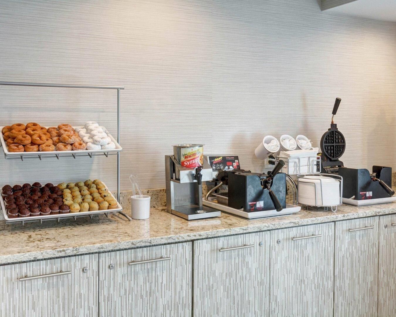 Un buffet pour le petit-déjeuner avec des viennoiseries, un distributeur de sirop et une machine à gaufres.