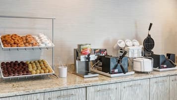 A breakfast bar with pastries, a syrup dispenser, and a waffle maker.