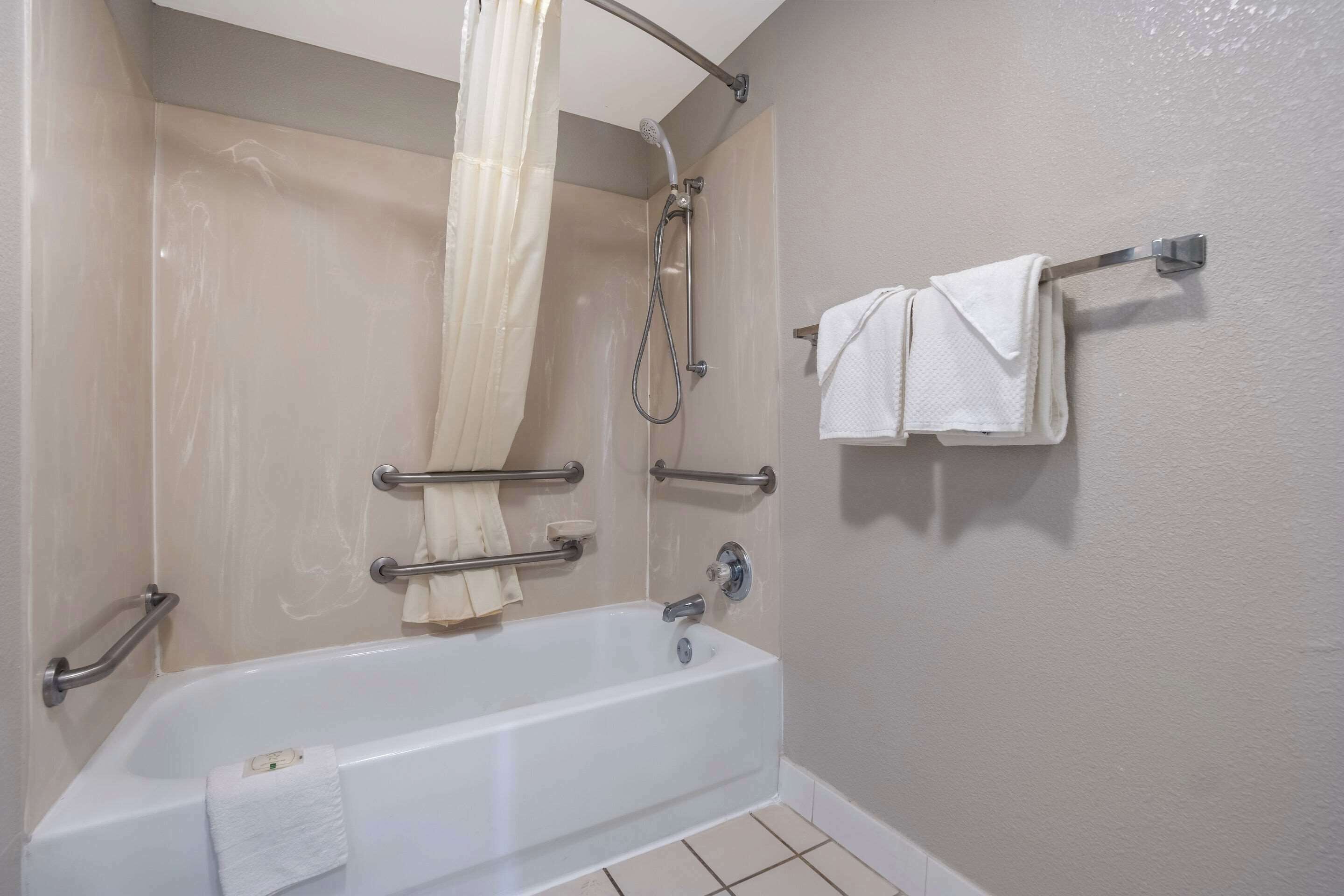 A bathroom with a bathtub, a shower, grab bars, a towel rack, and a curtain.