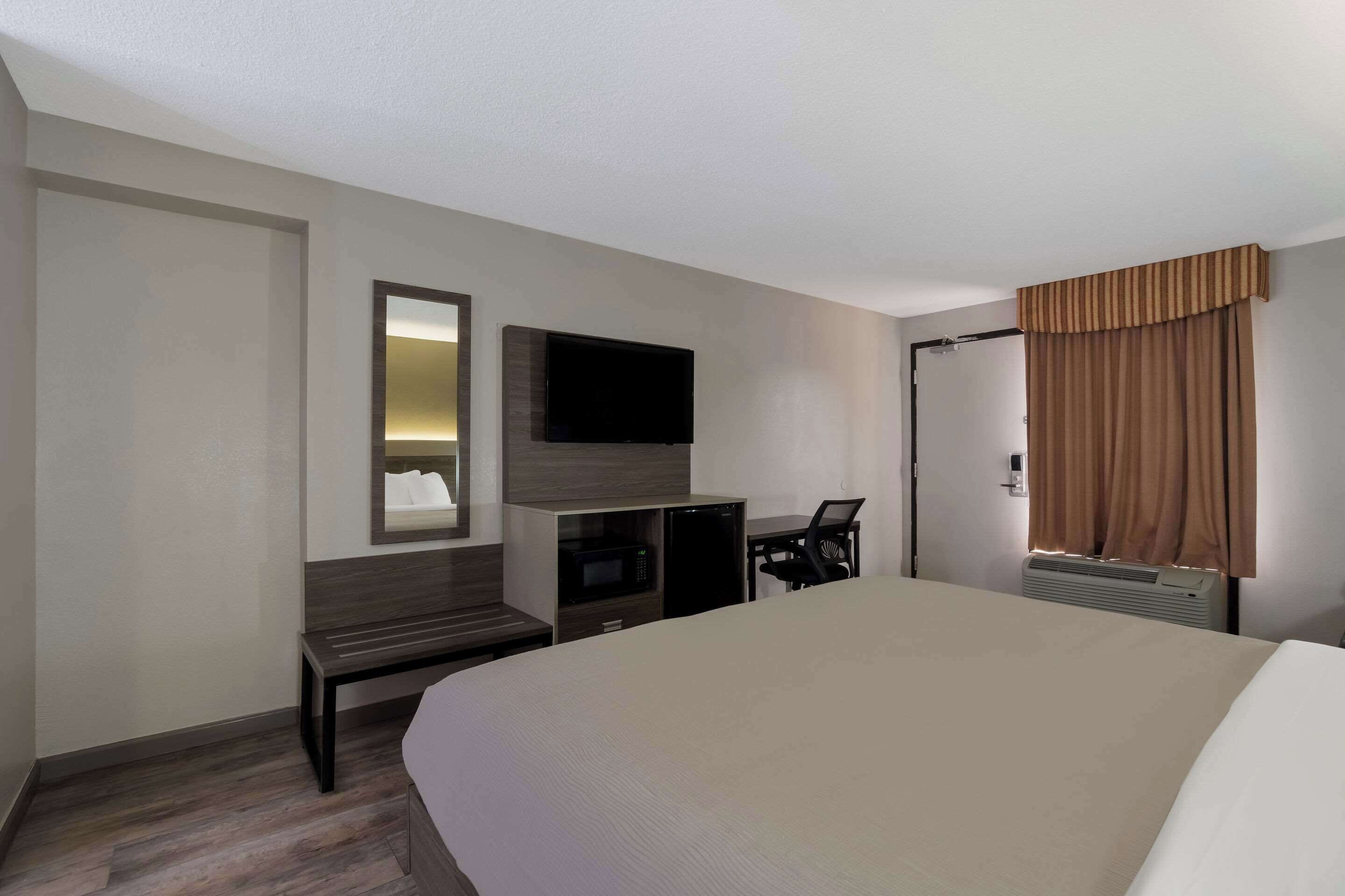 Habitación de hotel con una cama grande, un televisor de pantalla plana montado en la pared, un escritorio con una silla, un microondas y un calentador.