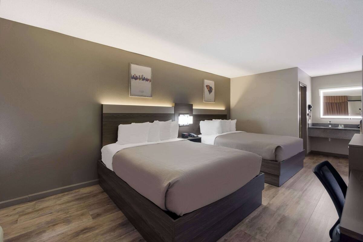 A hotel room with two beds, a desk, and a mirror.