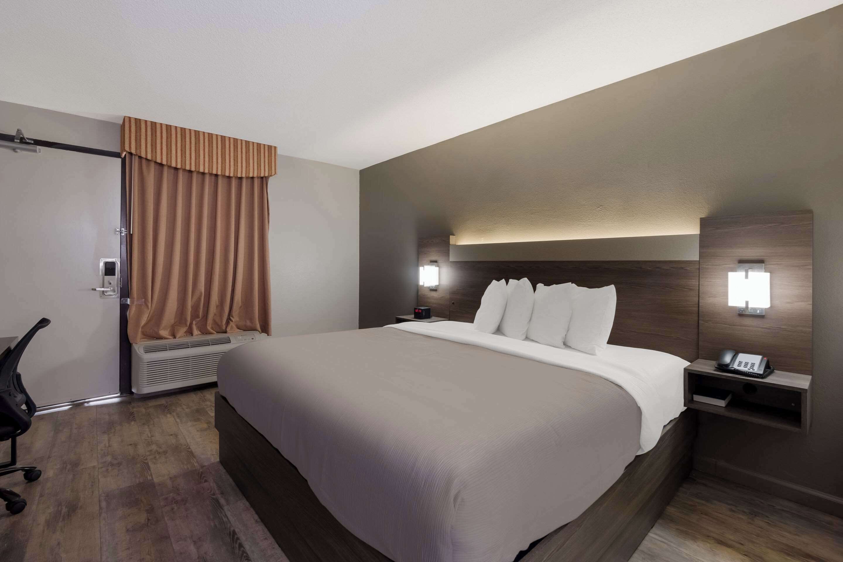 A hotel room with a large bed, a desk with a telephone, and a chair.