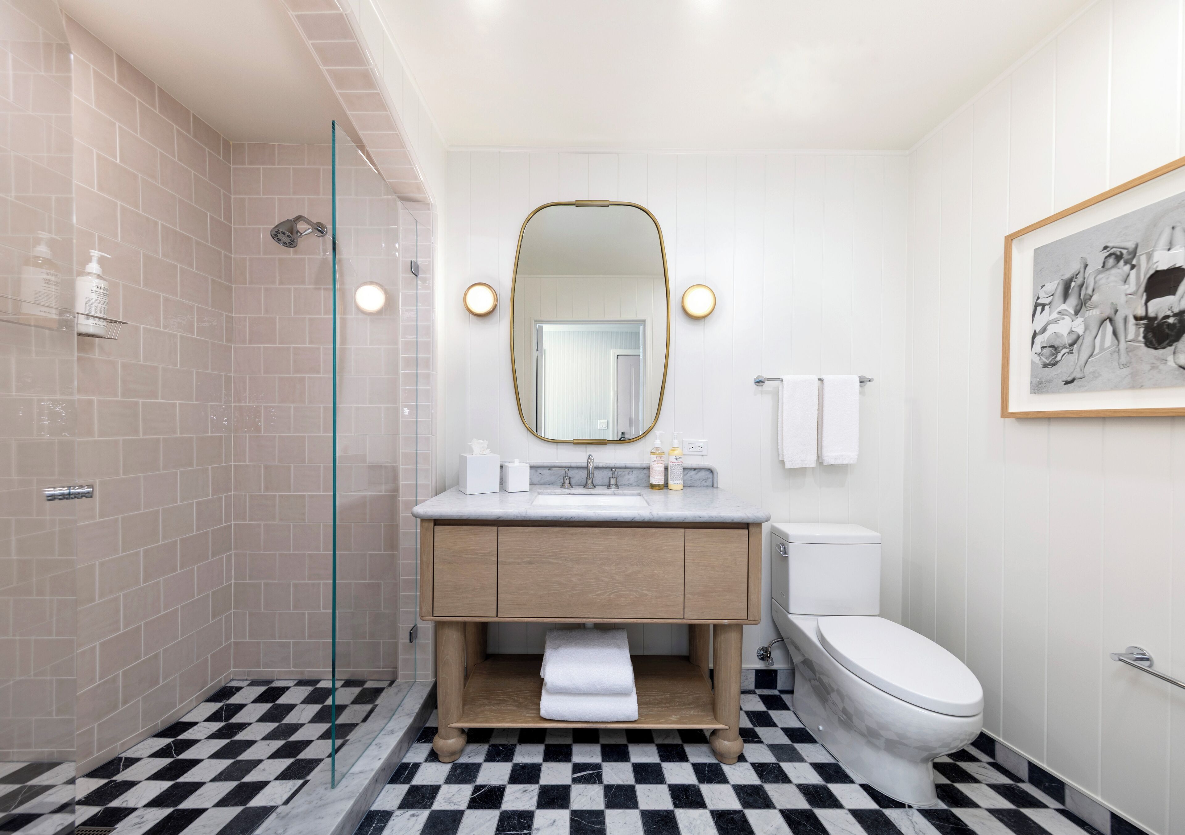 A modern bathroom with a checkered floor, a glass shower enclosure, a white sink with a gold mirror, and a toilet.