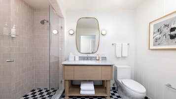 A modern bathroom with a checkered floor, a glass shower enclosure, a white sink with a gold mirror, and a toilet.